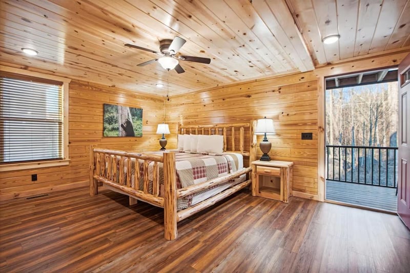 Unwind in your rustic log bedroom with handcrafted furnishings, cozy lighting, and a private balcony overlooking peaceful trees.