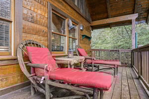 Unwind on your private covered deck with rustic lounge chairs and vibrant cushions, surrounded by lush forest views.