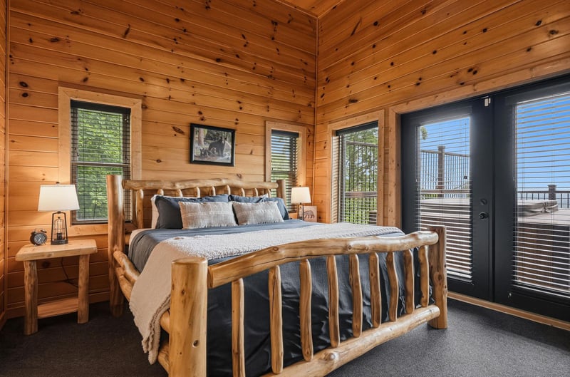 Unwind in your private bedroom retreat featuring a handcrafted log bed, warm pine walls, and doors opening to your own balcony with sweeping mountain vistas.