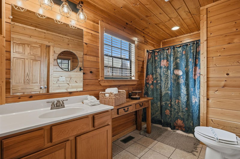 Unwind in your rustic bathroom with warm wood walls, elegant pendant lights, and charming details that create a cozy cabin retreat.