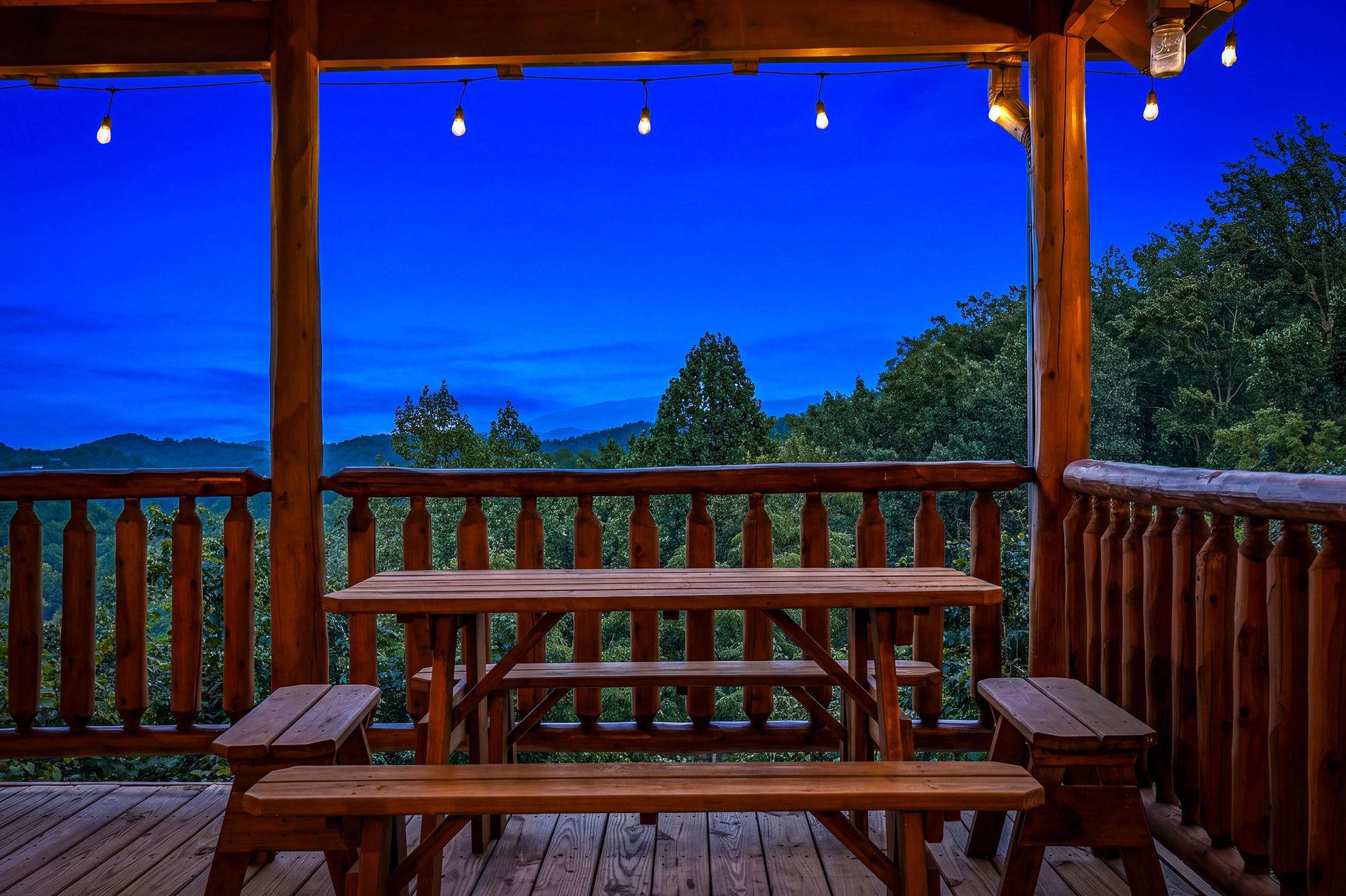 A tranquil mountain retreat captured at dusk, where rolling hills meet a vivid twilight sky. Your private deck offers a peaceful vantage point surrounded by lush forest, perfect for unwinding after a 