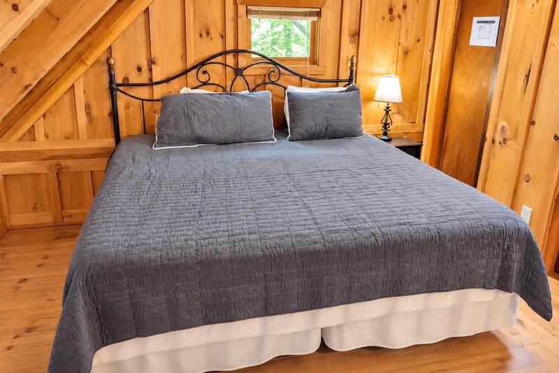 Curl up under warm quilts in your rustic cabin bedroom, where knotty pine walls and soft lamplight create the perfect cozy retreat after a day of exploring.