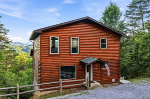 Twostory log cabin nestled among trees with mountain views, offering a peaceful retreat surrounded by lush greenery and scenic landscapes.