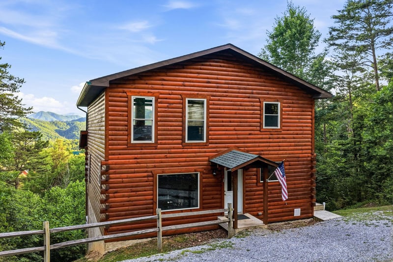 Twostory log cabin nestled among trees with mountain views, offering a peaceful retreat surrounded by lush greenery and scenic landscapes.
