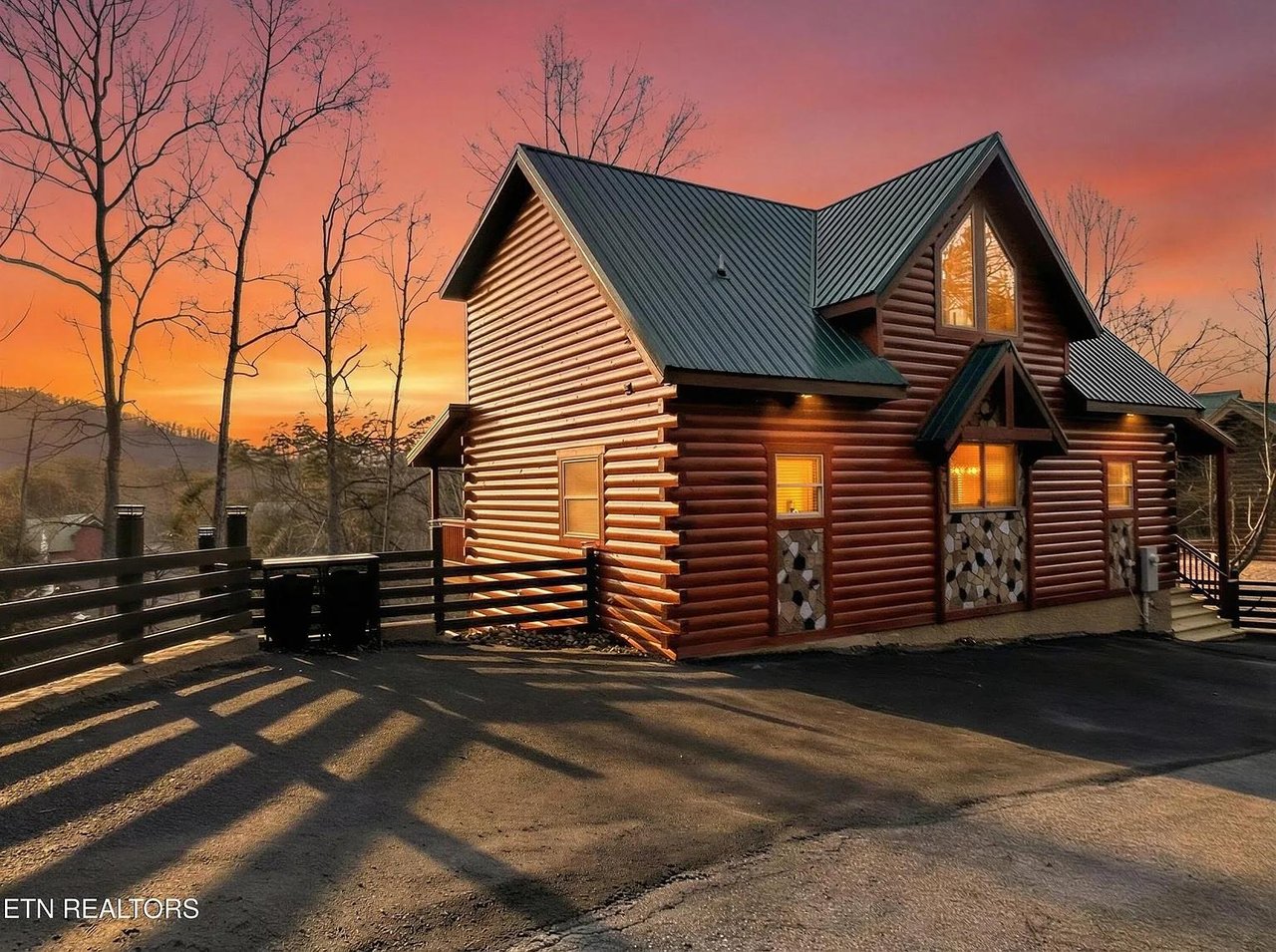 Rustic log cabin exterior with warm lighting at sunset, surrounded by natural landscape and parking area.