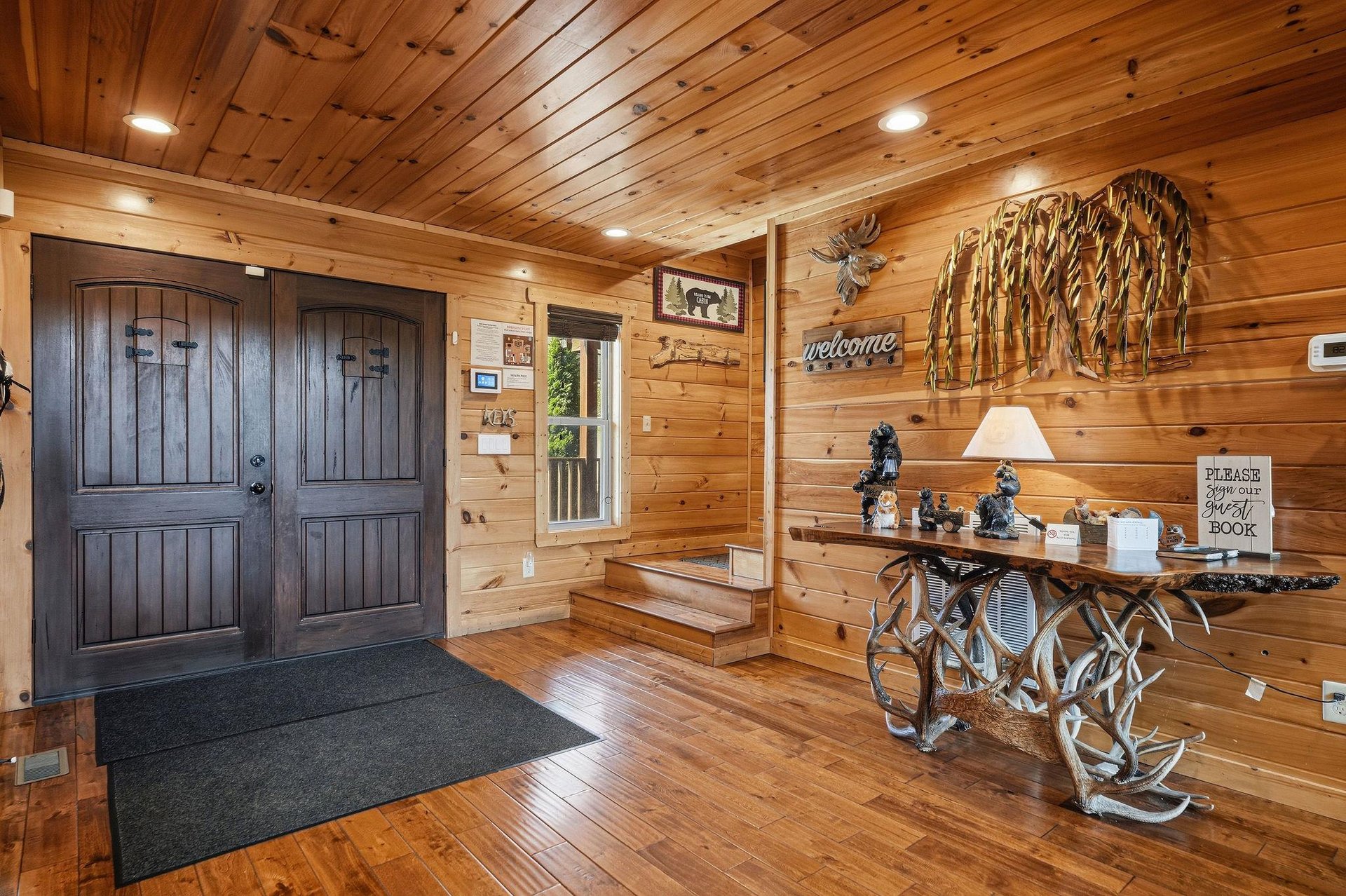 The entrance welcomes you with rustic charm—gleaming wood walls, a cozy welcome sign, and thoughtful décor that sets the tone for your mountain retreat.