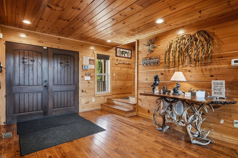 The entrance welcomes you with rustic charm—gleaming wood walls, a cozy welcome sign, and thoughtful décor that sets the tone for your mountain retreat.