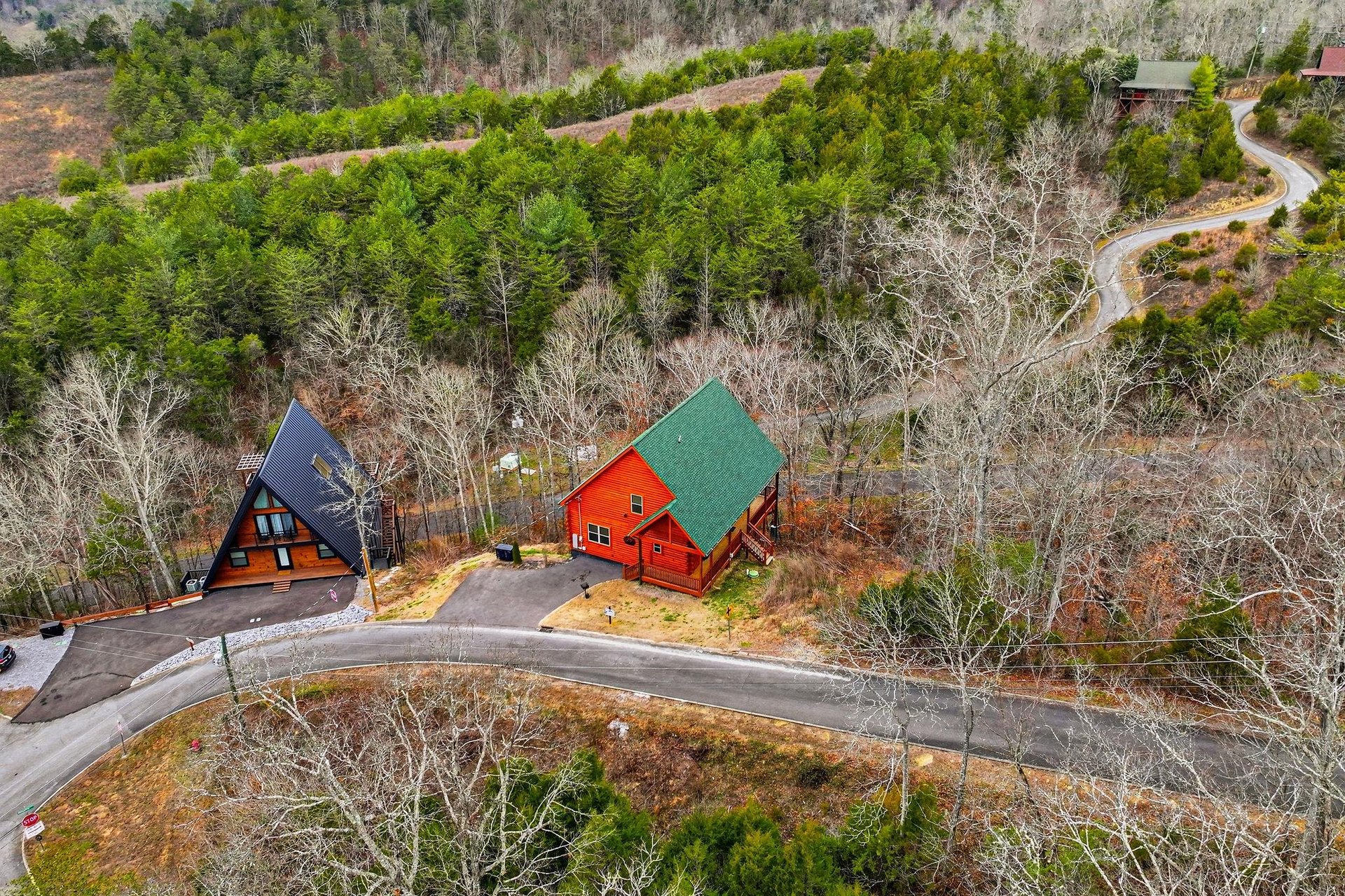 Aerial view of distinctive Aframe and cabinstyle properties nestled among rolling hills and winding mountain roads in a peaceful wooded setting.