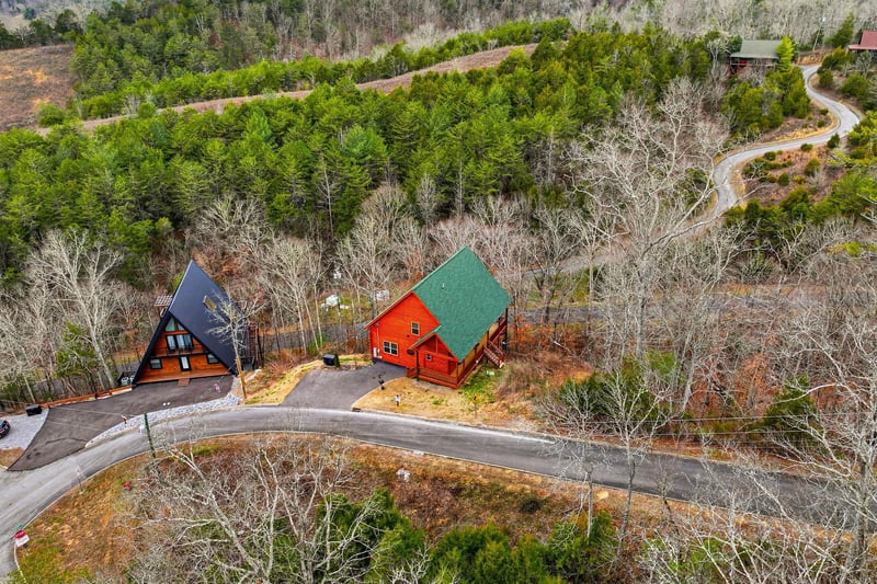 Aerial view of distinctive Aframe and cabinstyle properties nestled among rolling hills and winding mountain roads in a peaceful wooded setting.