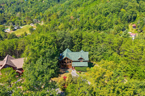 An aerial view captures the property nestled among lush forest, offering a secluded mountain escape with natural beauty all around.
