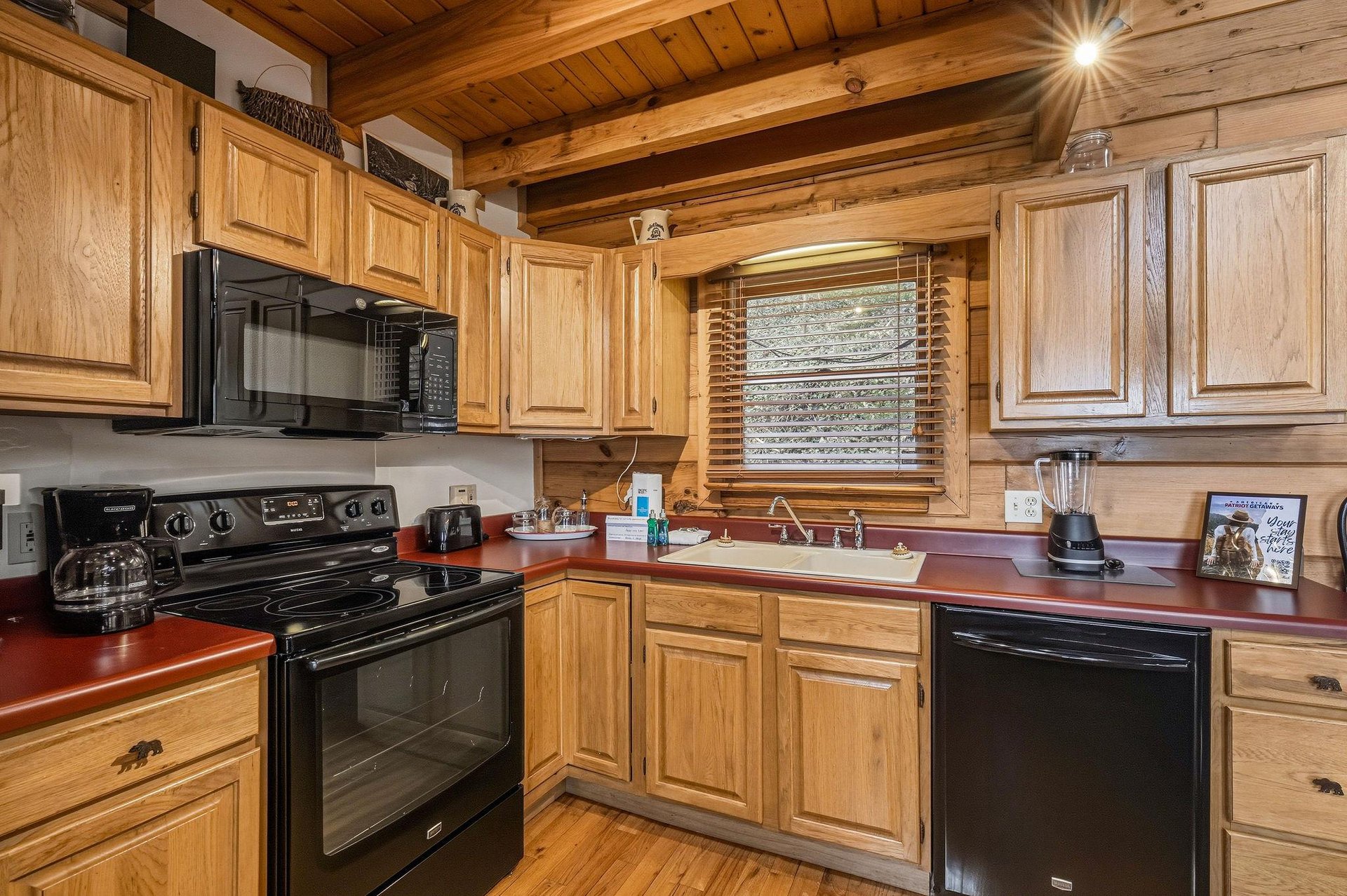 Your rustic cabin kitchen feels warm and welcoming with honey oak cabinets and exposed wooden beams overhead.