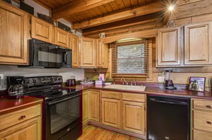 Your rustic cabin kitchen feels warm and welcoming with honey oak cabinets and exposed wooden beams overhead.