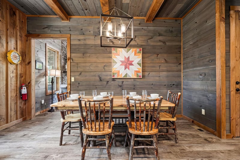 Gather with loved ones around the farmhouse table in this cozy dining space, where rustic wood walls, vaulted beamed ceilings, and a handcrafted lantern create a warm, inviting atmosphere for memorabl