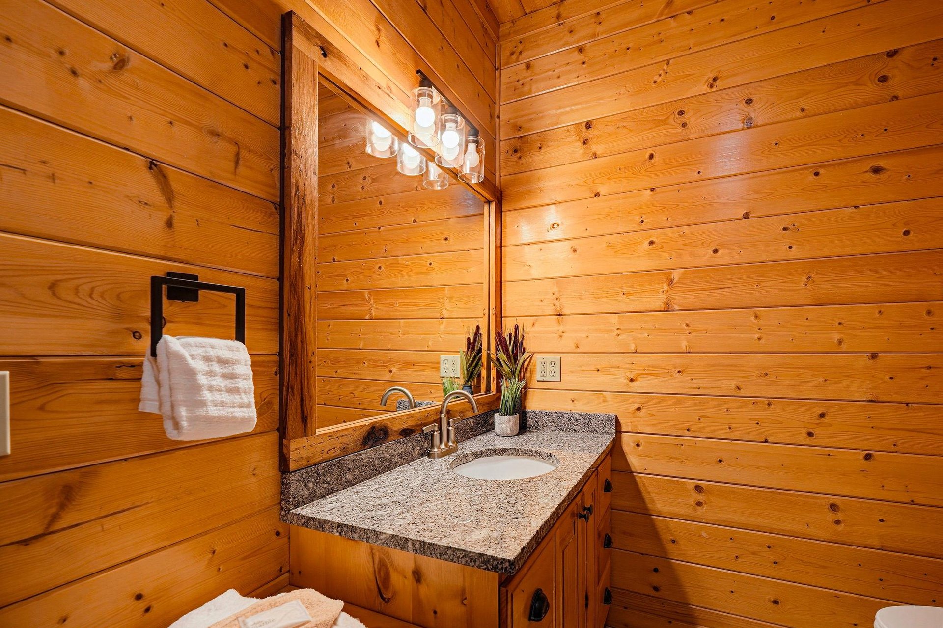 Step into your rustic bathroom retreat with warm wood walls, granite countertop, and charming mason jar lighting that creates the perfect cabin ambiance.