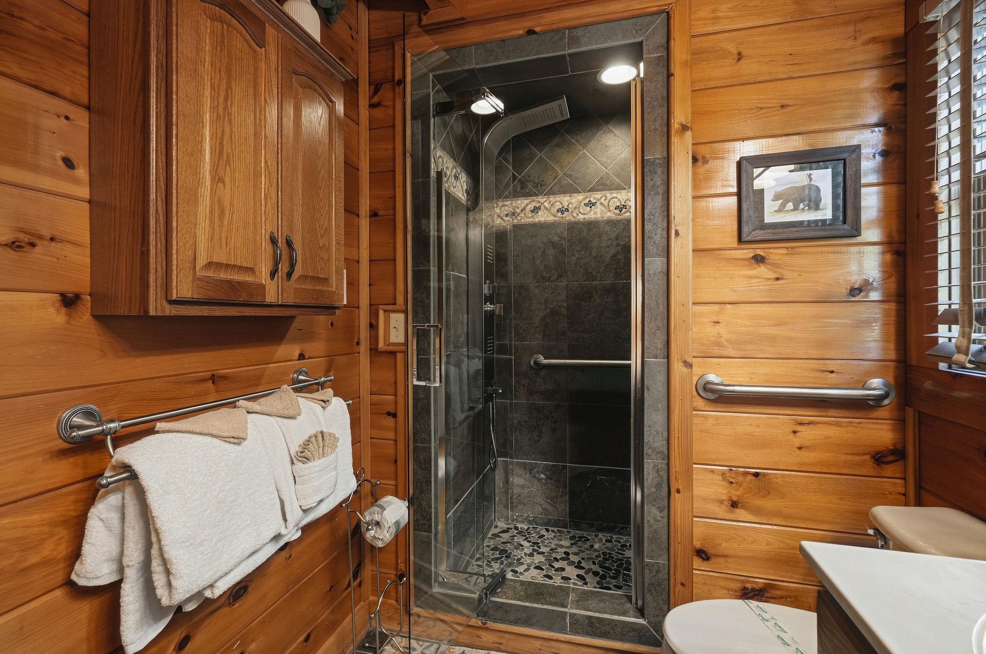 Step into your rustic bathroom featuring warm wood walls, a luxurious stone shower, and thoughtful accessibility features for comfort.