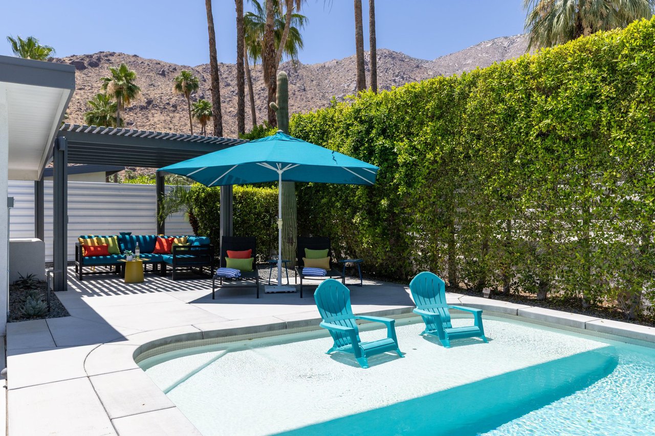 View of pergola with shaded outdoor seating and shallow end in pool.