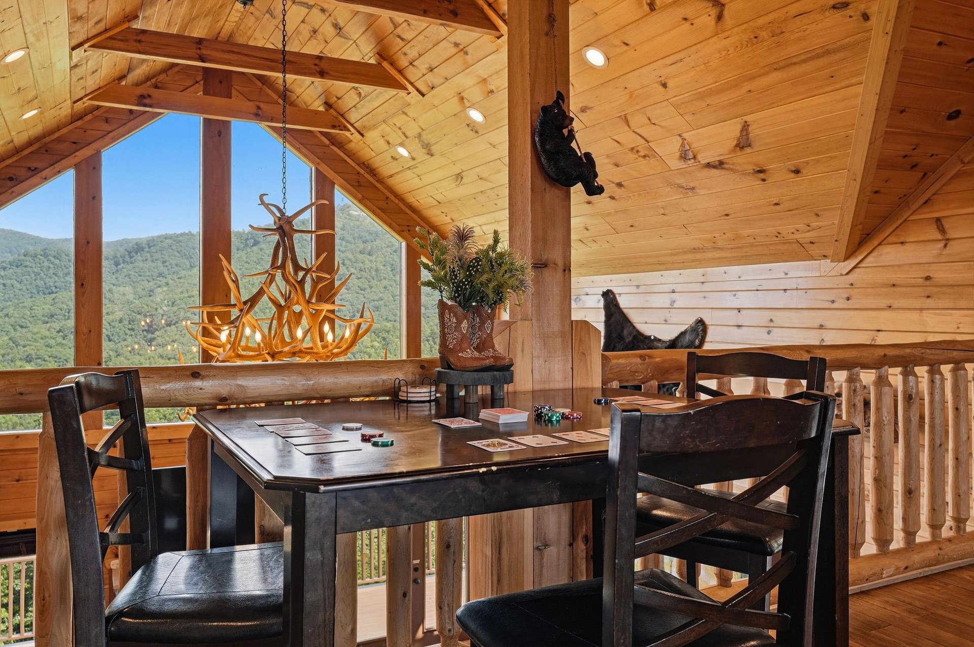 Stunning mountain views frame your dining space in this openloft cabin with exposed wood beams and rustic charm. Sunlight floods the room through dramatic vaulted windows.