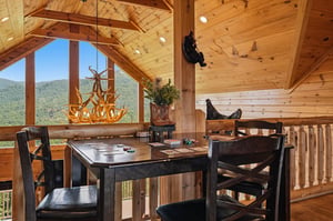 Stunning mountain views frame your dining space in this openloft cabin with exposed wood beams and rustic charm. Sunlight floods the room through dramatic vaulted windows.
