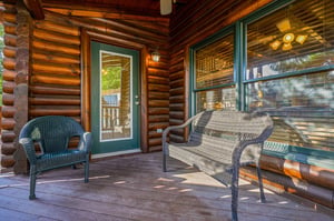 Step onto your private porch and settle into cozy wicker seating surrounded by warm, rustic log cabin charm—your perfect retreat for morning coffee or evening relaxation.