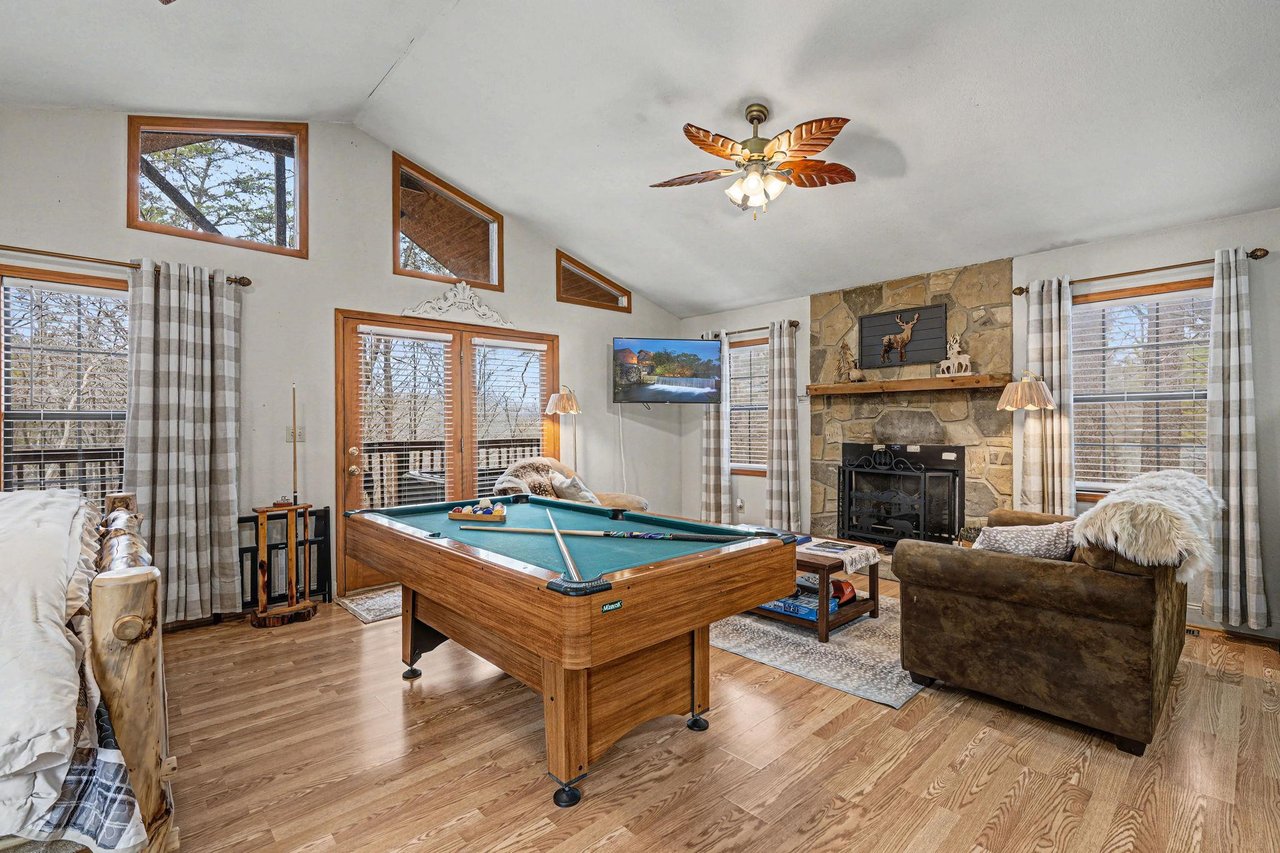 Your cozy game room features a pool table and stone fireplace, perfect for evening entertainment with forest views.