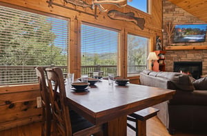 Your cozy cabin retreat blends rustic charm with mountain comfort. Gather around the wood dining table, relax by the fireplace, and take in the stunning mountain views through expansive windows.