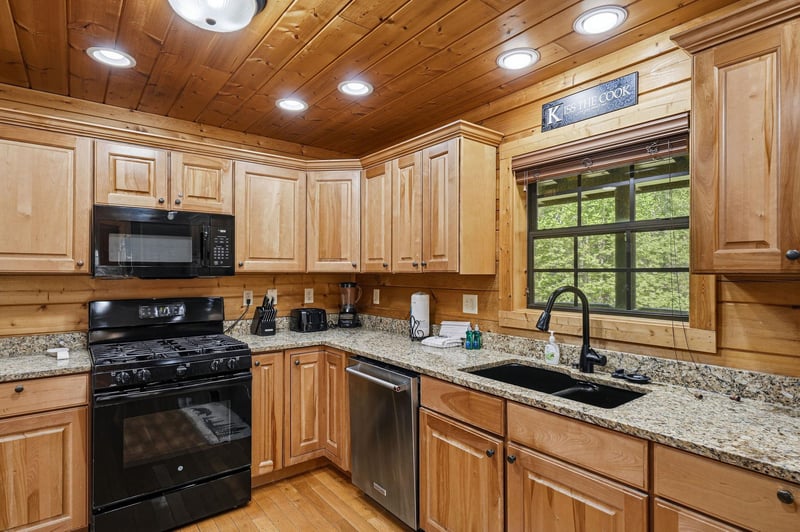 Your fully equipped kitchen features granite counters, gas stove, and dishwasher  perfect for preparing meals while enjoying forest views.