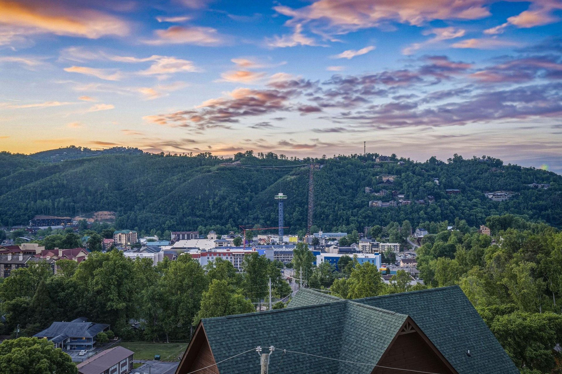 Elevated view showcasing the propertys hillside location amid lush greenery, with vibrant downtown attractions and forested mountains forming a picturesque backdrop.