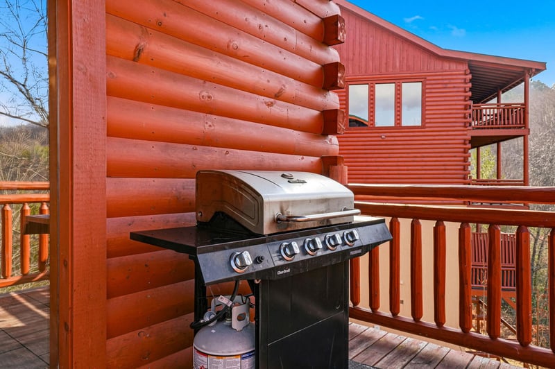 Your private deck awaits with a premium gas grill ready for mountain cookouts surrounded by stunning log cabin architecture.