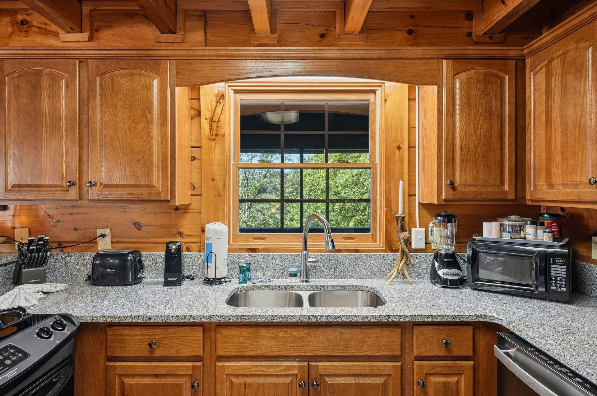 Your fully equipped kitchen features granite countertops, rich wood cabinetry, and a window overlooking peaceful greenery—perfect for preparing meals in rustic elegance.