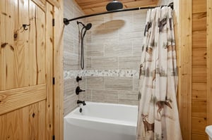 Unwind in your rustic bathroom featuring a modern tubshower combo with rainfall showerhead and charming wildlifethemed curtain.