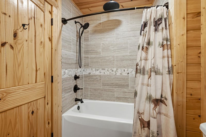 Unwind in your rustic bathroom featuring a modern tubshower combo with rainfall showerhead and charming wildlifethemed curtain.