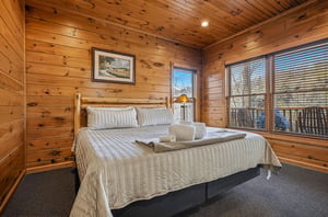 Drift off in your cozy cabinstyle bedroom, featuring warm knotty pine walls, a plush bed with fresh linens, and windows that frame peaceful woodland views.