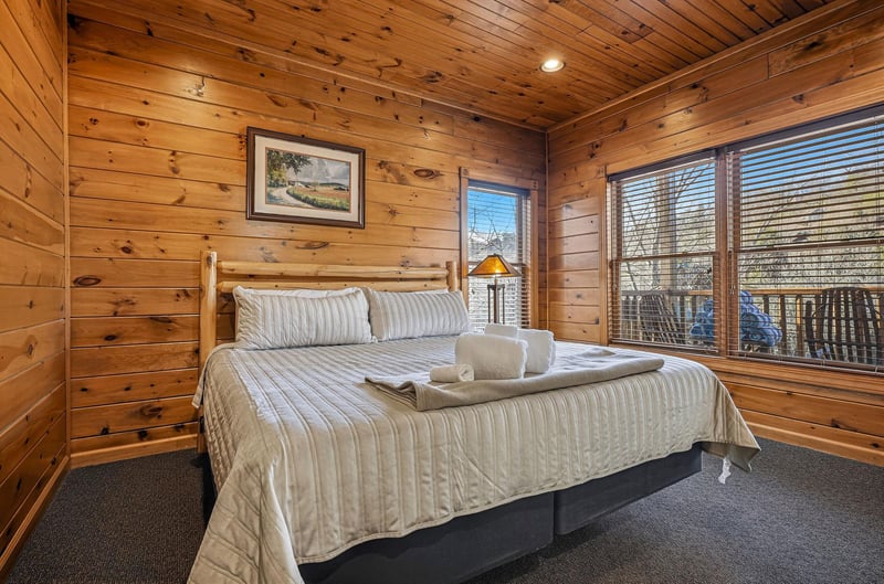 Drift off in your cozy cabinstyle bedroom, featuring warm knotty pine walls, a plush bed with fresh linens, and windows that frame peaceful woodland views.