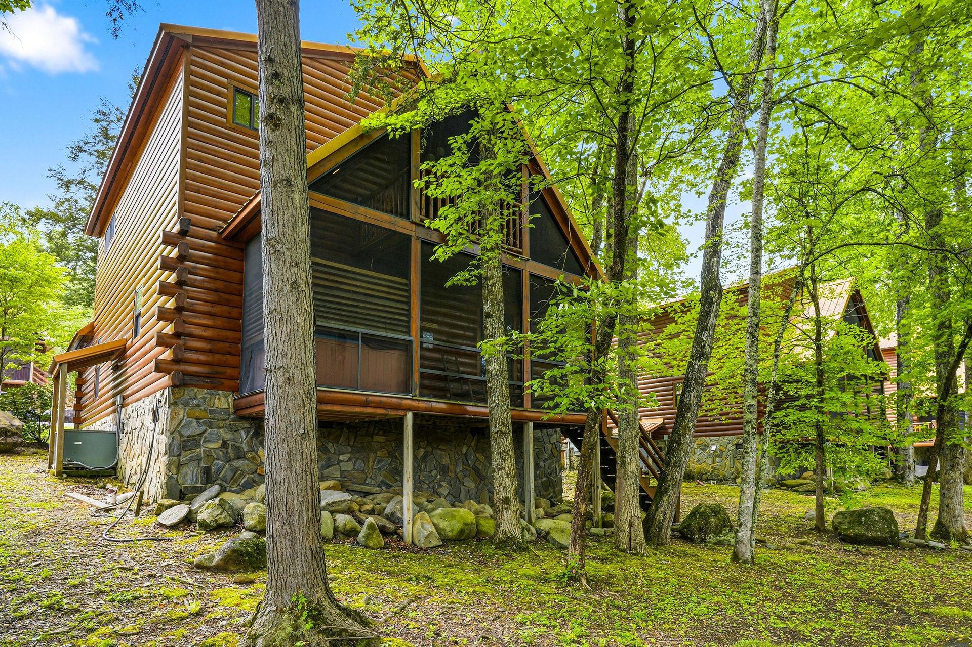 Charming log cabin nestled among towering trees offers a peaceful forest retreat with rustic stone foundation and inviting covered porches.
