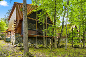Charming log cabin nestled among towering trees offers a peaceful forest retreat with rustic stone foundation and inviting covered porches.