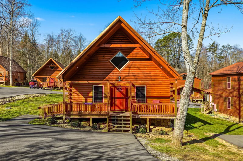 Charming log cabin features warm wood exterior with inviting front porch in peaceful wooded setting.