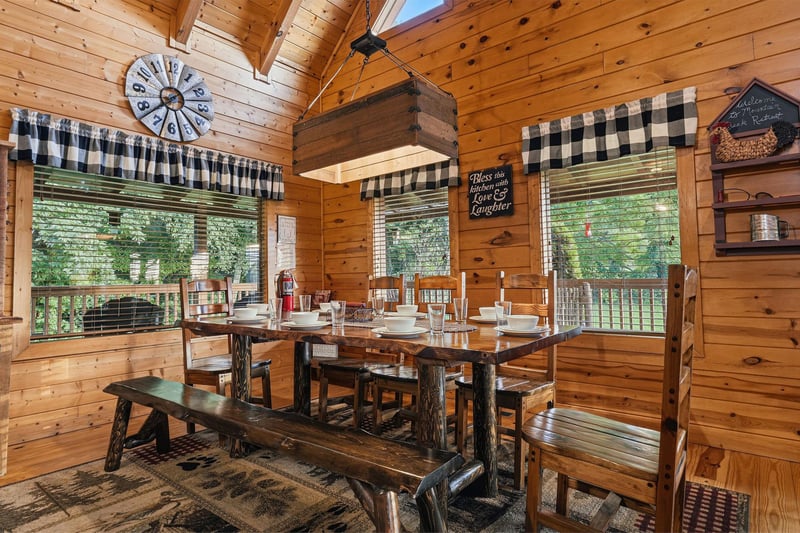Gather around the rustic log table for memorable meals under the warmth of wood beams and natural light streaming through large windows overlooking peaceful greenery.