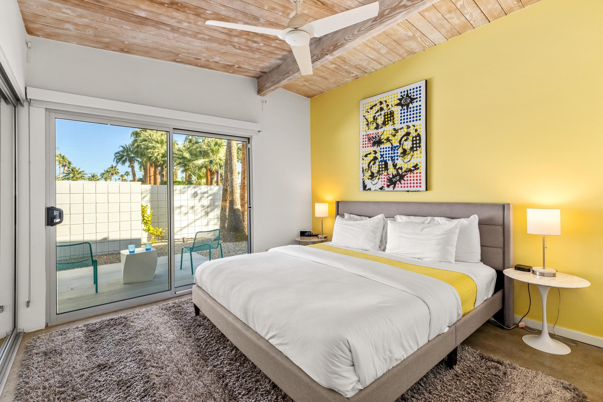Wake up in your vibrant bedroom where wood beams create warmth above and your private patio beckons just beyond sliding doors.