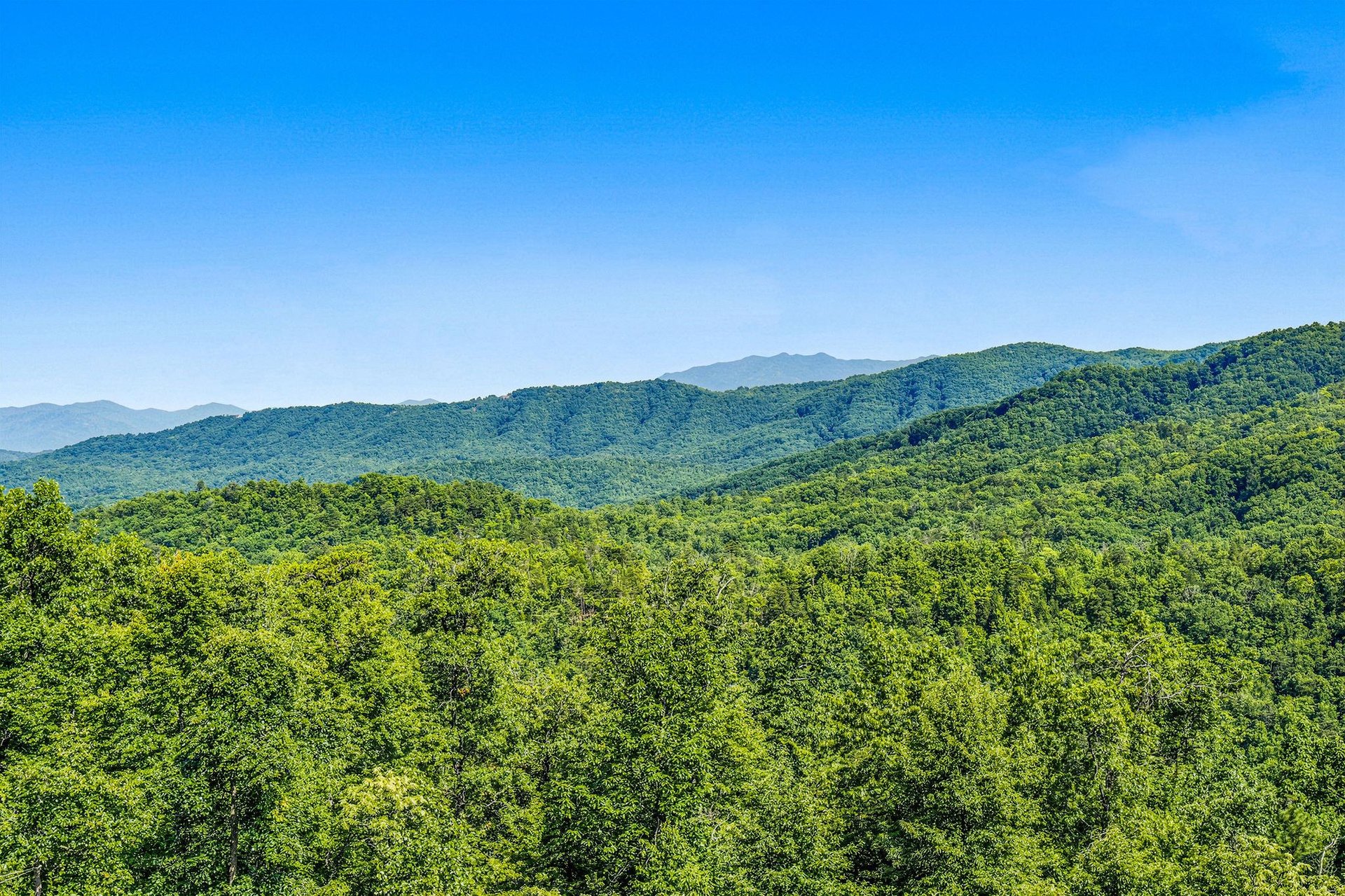 Sweeping panorama of forested mountains and ridges stretching toward the horizon under a brilliant blue sky, capturing the natural beauty surrounding the property.