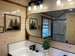 Unwind in your rusticchic bathroom featuring charming mountain artwork, elegant white stone backsplash, and spacious glass shower with natural light streaming in.