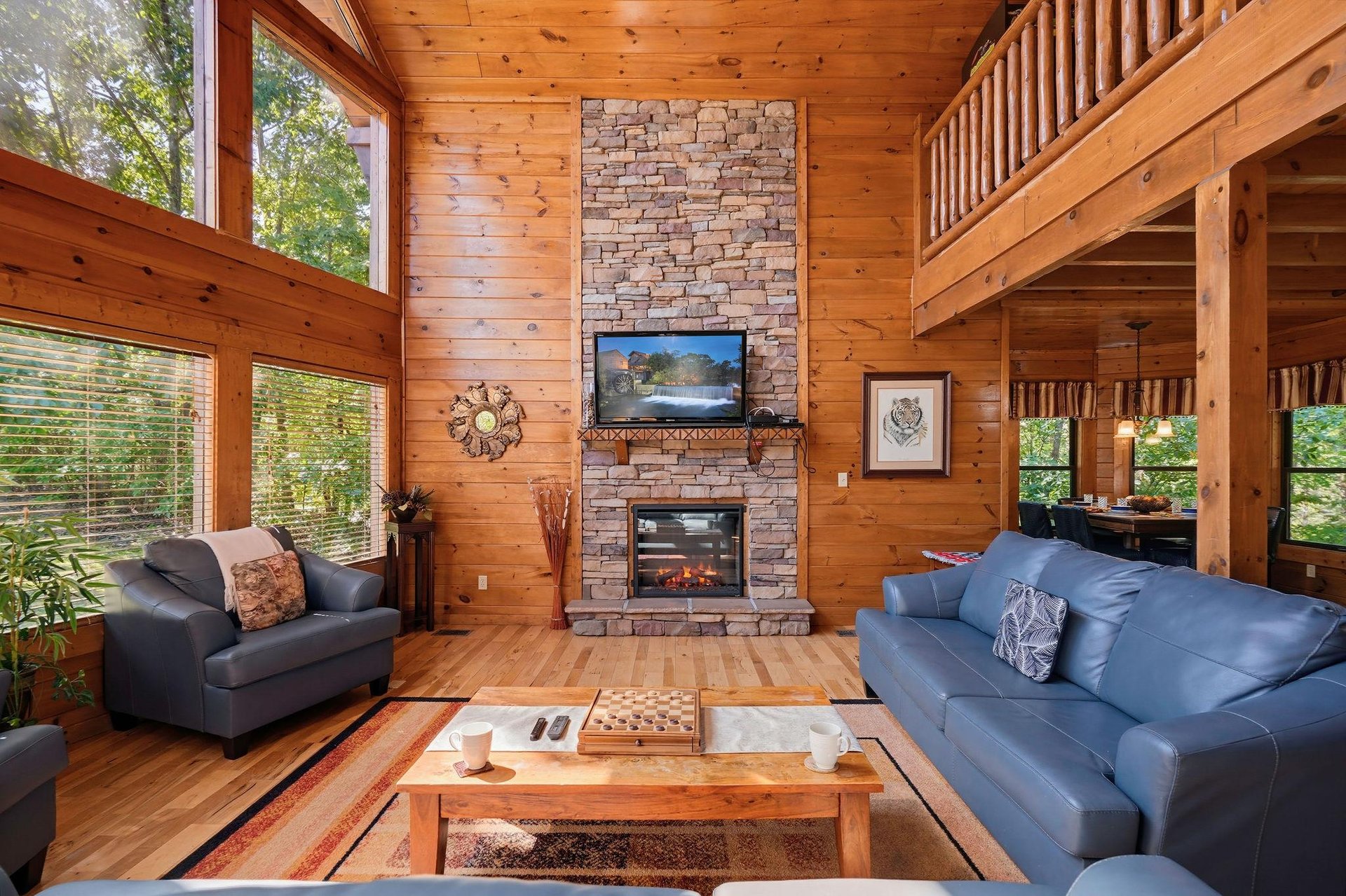Unwind in your inviting living room, where warm wood surrounds you and natural light pours in through expansive windows. Cozy up by the stone fireplace as sunlight filters through the trees outside.