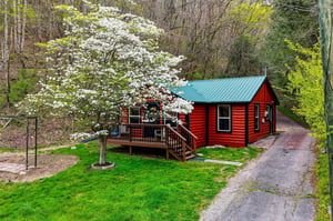 Charming red log cabin nestled among blooming dogwood trees offers a peaceful spring retreat with private deck and wooded setting.