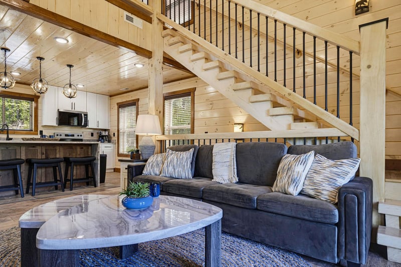 Sink into the plush sofa beneath soaring wood ceilings and natural light. Your modern cabin retreat features a full kitchen and airy open layout, perfect for unwinding after a day exploring.