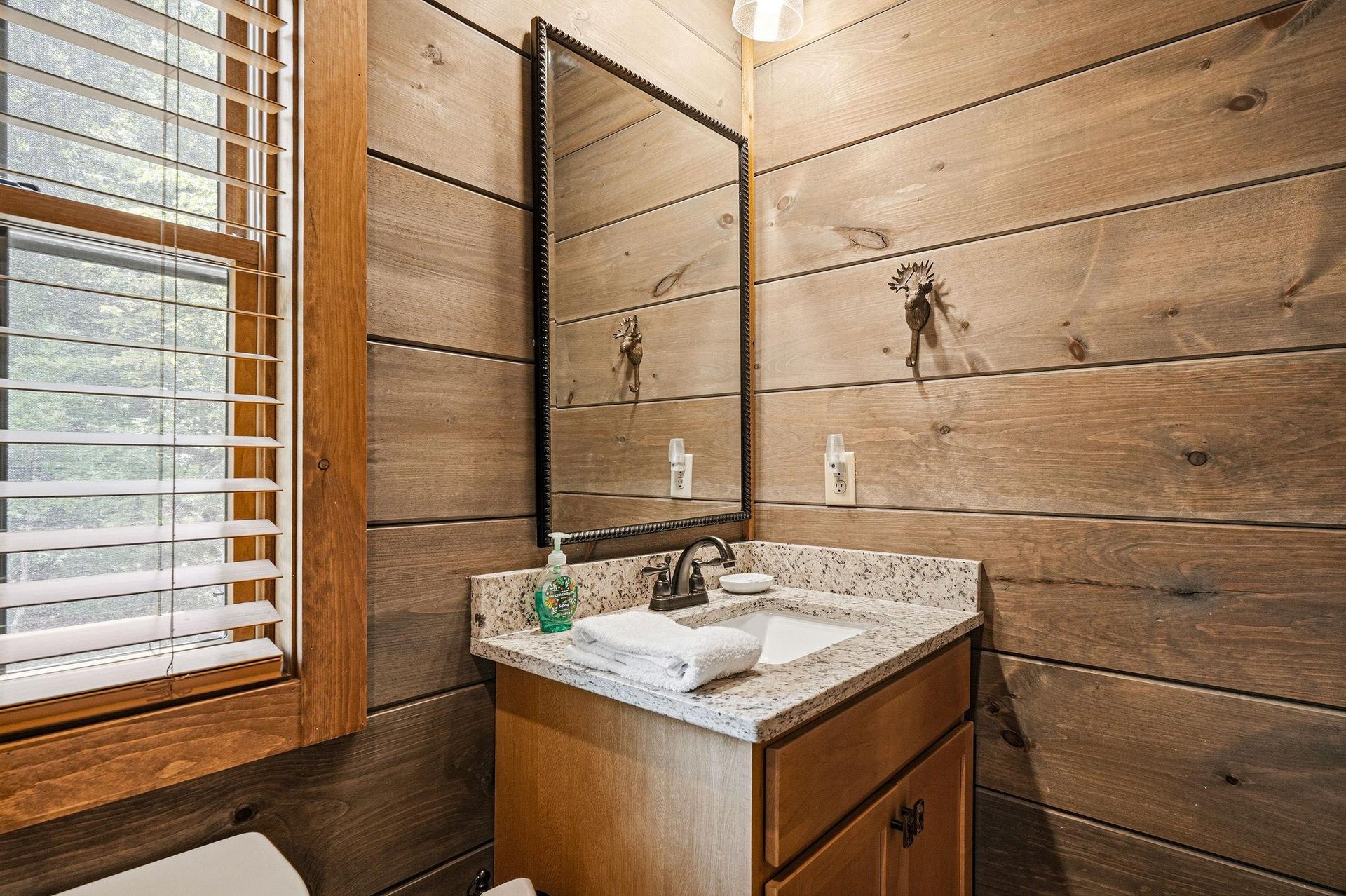Unwind in this cozy bathroom with warm wood walls, granite countertop, and rustic deerantler fixtures lending authentic cabin charm to your mountain retreat.