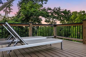A peaceful deck overlooks lush treetops as the sky glows with soft pink and purple hues at sunset, offering your perfect spot to unwind with nature.