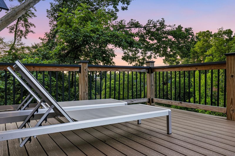 A peaceful deck overlooks lush treetops as the sky glows with soft pink and purple hues at sunset, offering your perfect spot to unwind with nature.