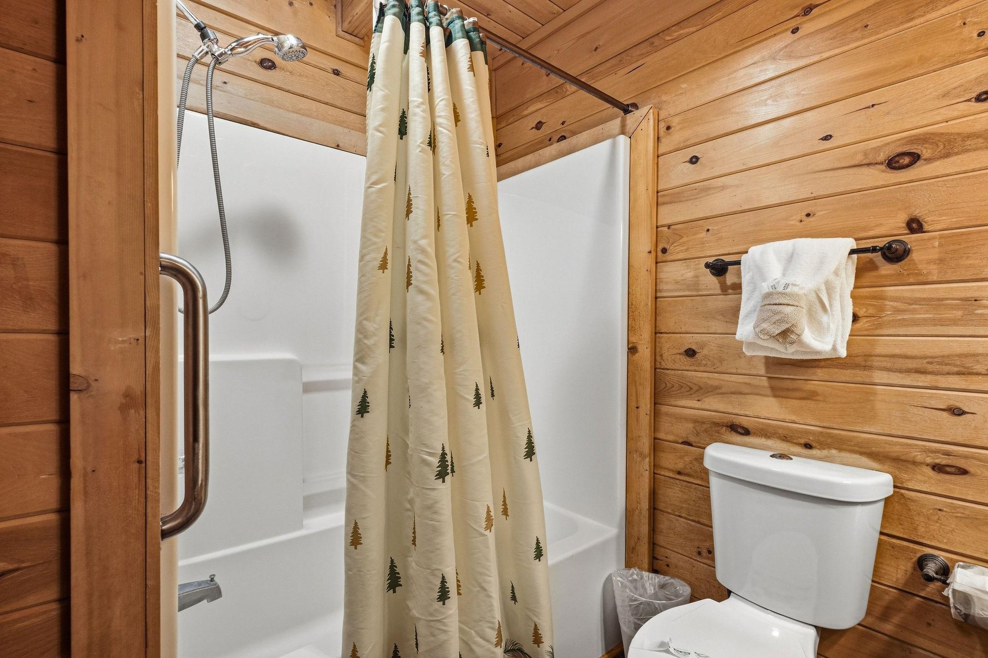Your rustic cabin bathroom features warm wood paneling and charming treepatterned curtains, creating a cozy mountain retreat atmosphere.