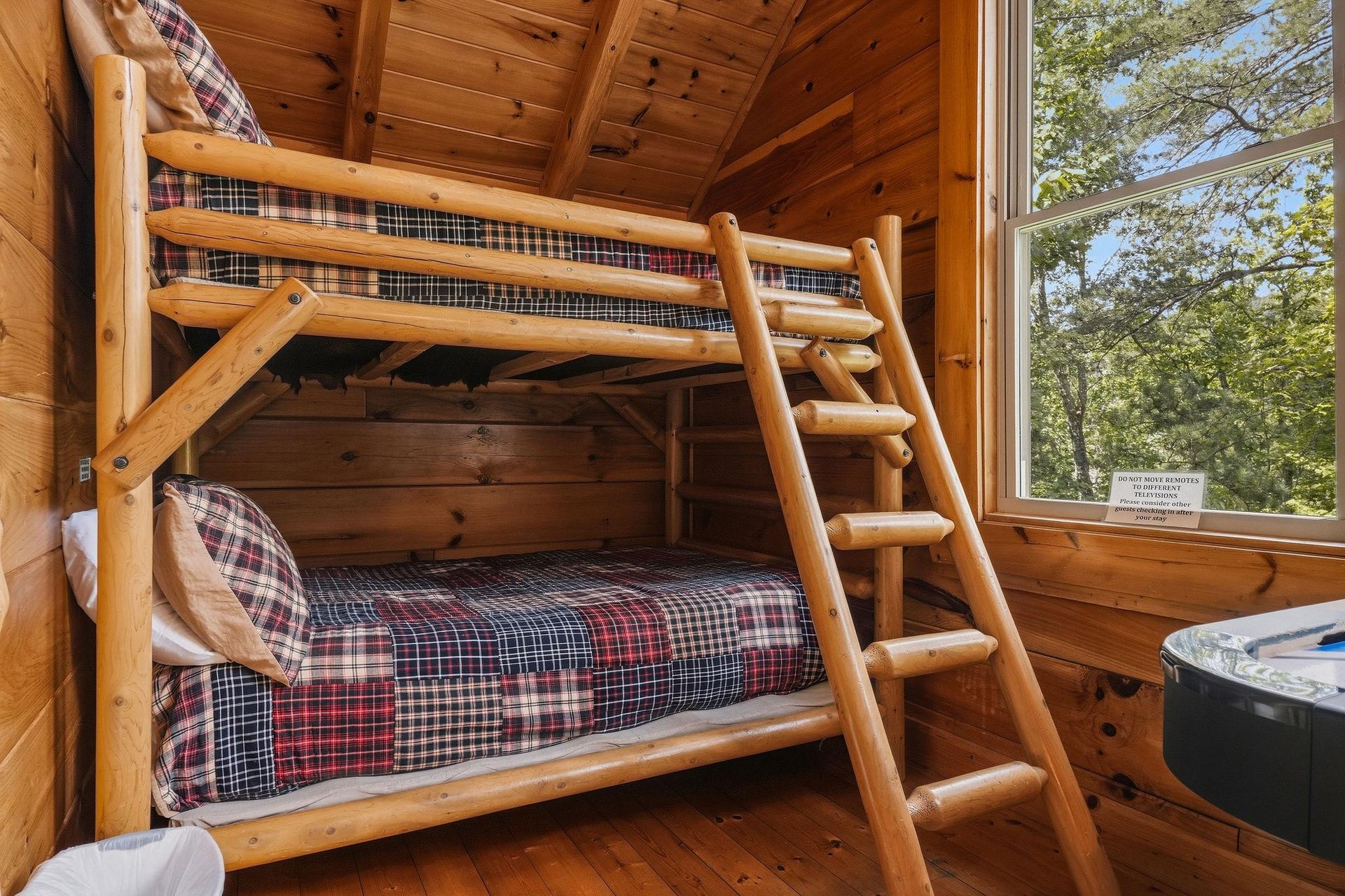 Rest easy in this charming log bunk room with warm wood accents and a peaceful view of the trees. A hot tub awaits nearby for your relaxation.