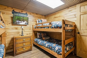 This cozy cabin bedroom features charming bunk beds with rustic wood detailing, perfect for younger adventurers. Natural light streams through the skylight above, illuminating warm pine walls and crea