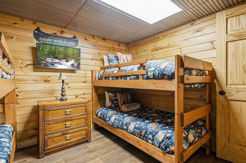This cozy cabin bedroom features charming bunk beds with rustic wood detailing, perfect for younger adventurers. Natural light streams through the skylight above, illuminating warm pine walls and crea